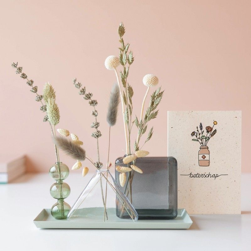 Drie verschillende vaasjes met droogbloemen op een plateau met daarnaast een beterschap wenskaart