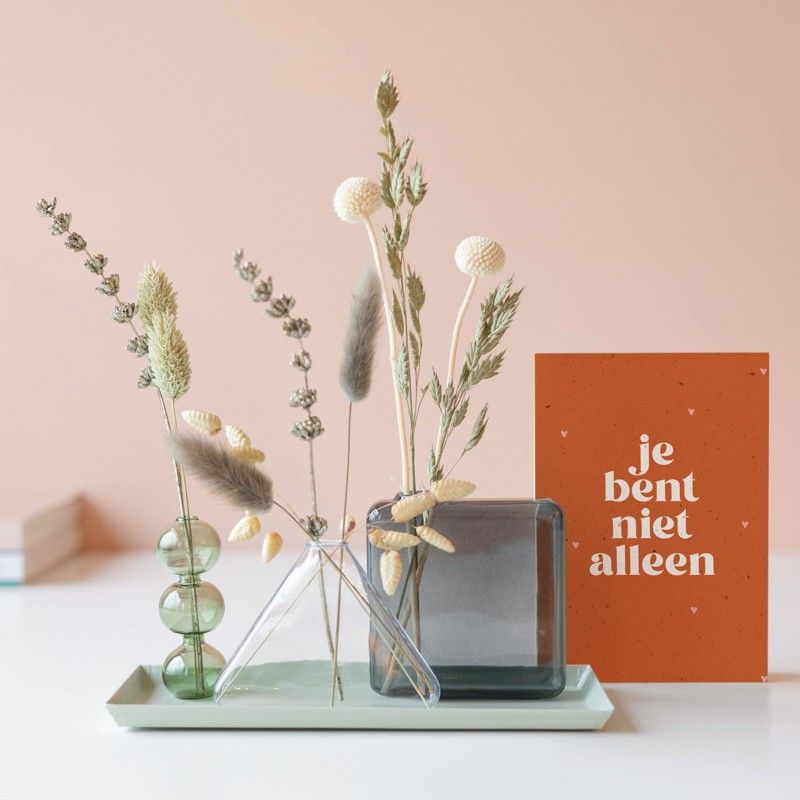 Drie verschillende vaasjes met droogbloemen op een plateau met een je bent niet alleen wenskaart ernaast