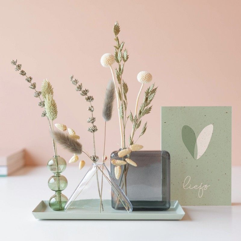 Naturel droogbloemen in drie verschillende vaasjes op een plateau met een wenskaart ernaast waar liefs opgeschreven staat onder een wit groen hart