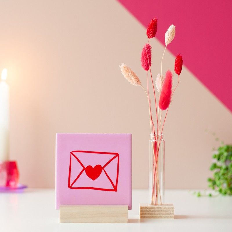 Close-up van roze en beige droogbloemen, met op de achtergrond het roze tegeltje met rode envelop illustratie.