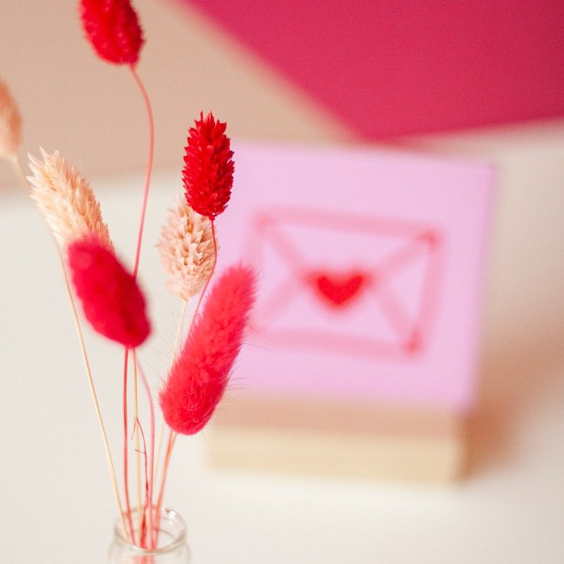 Close-up van roze en beige droogbloemen, met op de achtergrond het roze tegeltje met rode envelop illustratie.