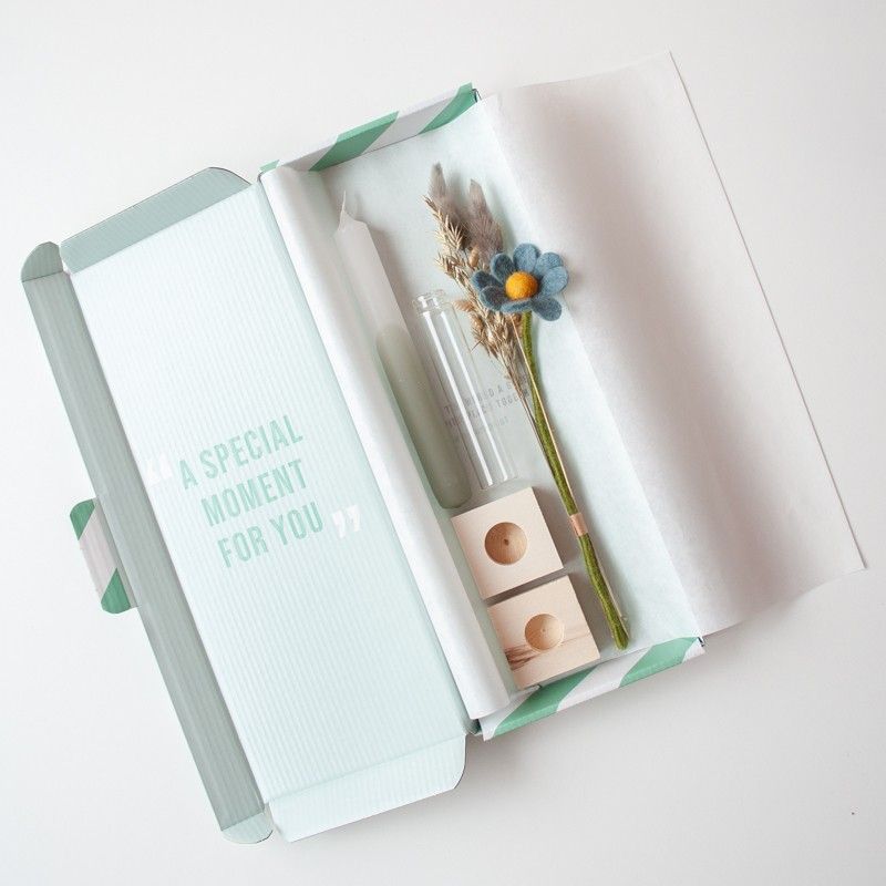 Brievenbuspakketje met wit groene kaars in een houten blokje met daarnaast een vaasje droogbloemen en vilten bloemen in een houten blokje