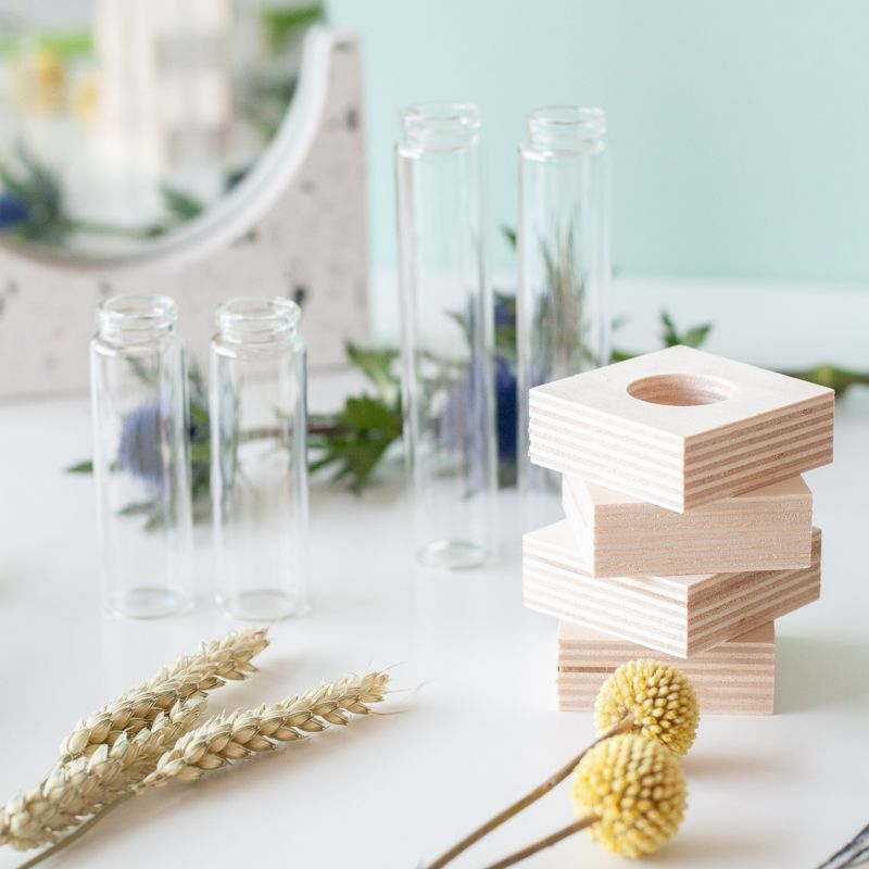 Brievenbuspakketje met vier vaasjes in houten blokjes met verschillende bloemen en een pauwenveer