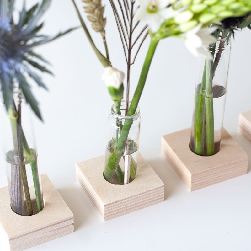 Brievenbuspakketje met vier vaasjes in houten blokjes met verschillende bloemen en een pauwenveer