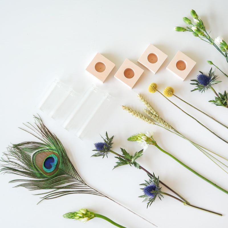 Brievenbuspakketje met vier vaasjes in houten blokjes met verschillende bloemen en een pauwenveer