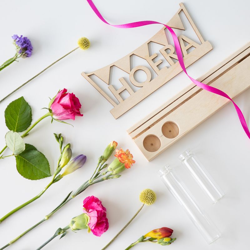 Brievenbuspakket met een houten plankje, houten hoera tekst en twee vaasjes met verse bloemen. Er is ruimte voor een wenskaart in de plank