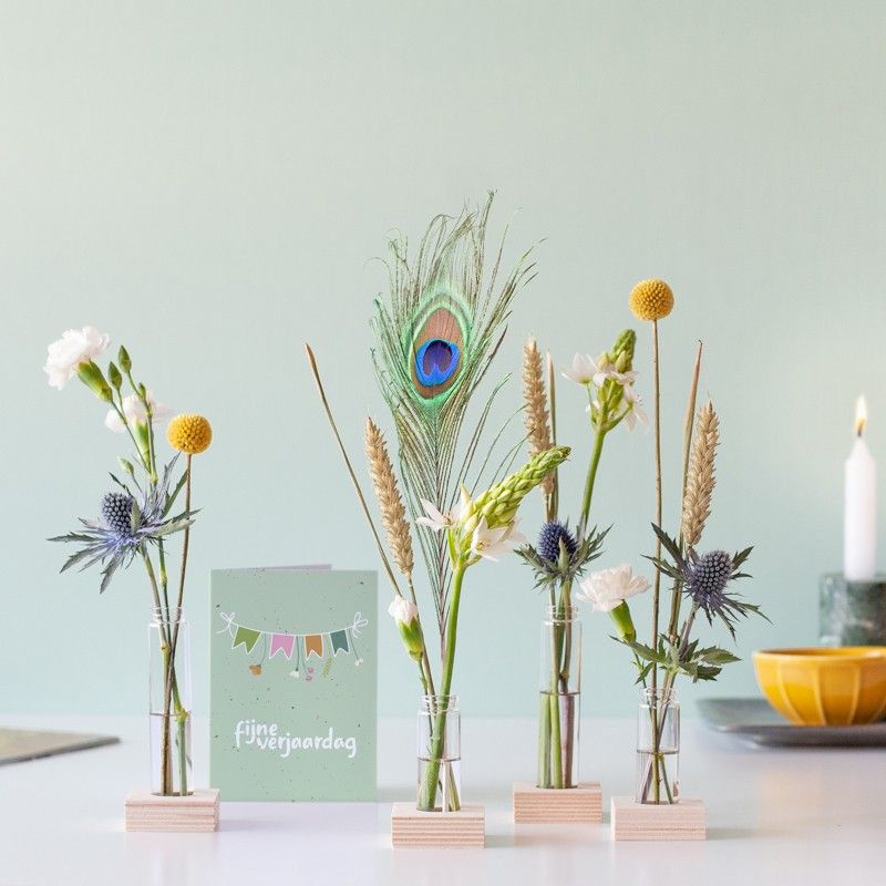 Brievenbuspakketje met vier vaasjes in houten blokjes met verschillende bloemen en een pauwenveer