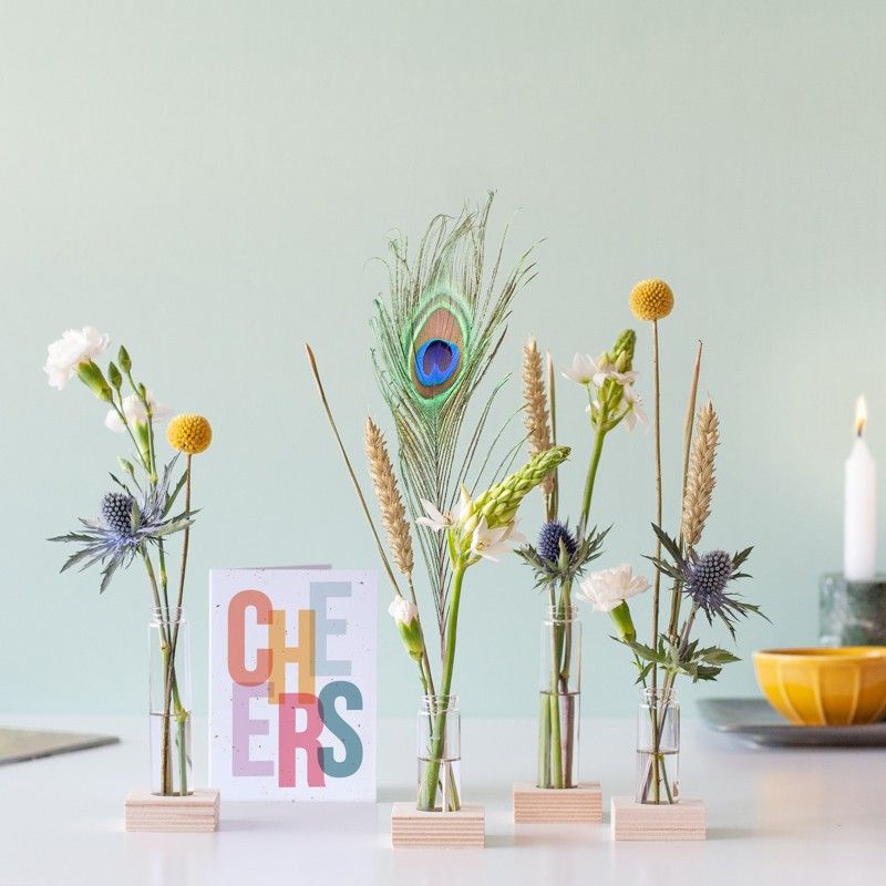 Brievenbuspakketje met vier vaasjes in houten blokjes met verschillende bloemen en een pauwenveer