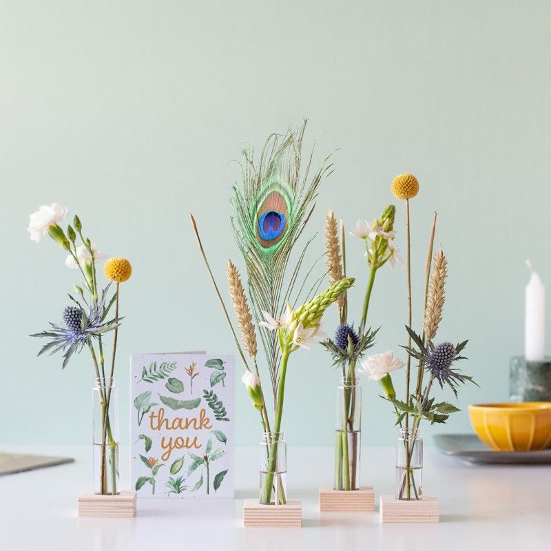 Brievenbuspakketje met vier vaasjes in houten blokjes met verschillende bloemen en een pauwenveer
