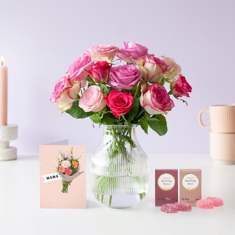 Roze brievenbusrozen in een transparante vaas met 2 doosjes winegums ernaast en een wenskaart met boeket en mam erop geschreven