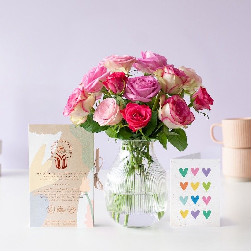 roze brievenbus rozen in verschillende roze tinten in een transparante vaas. Daarnaast staat een doosje met verzorgende maskers en een wenskaart met verschillende kleuren hartjes
