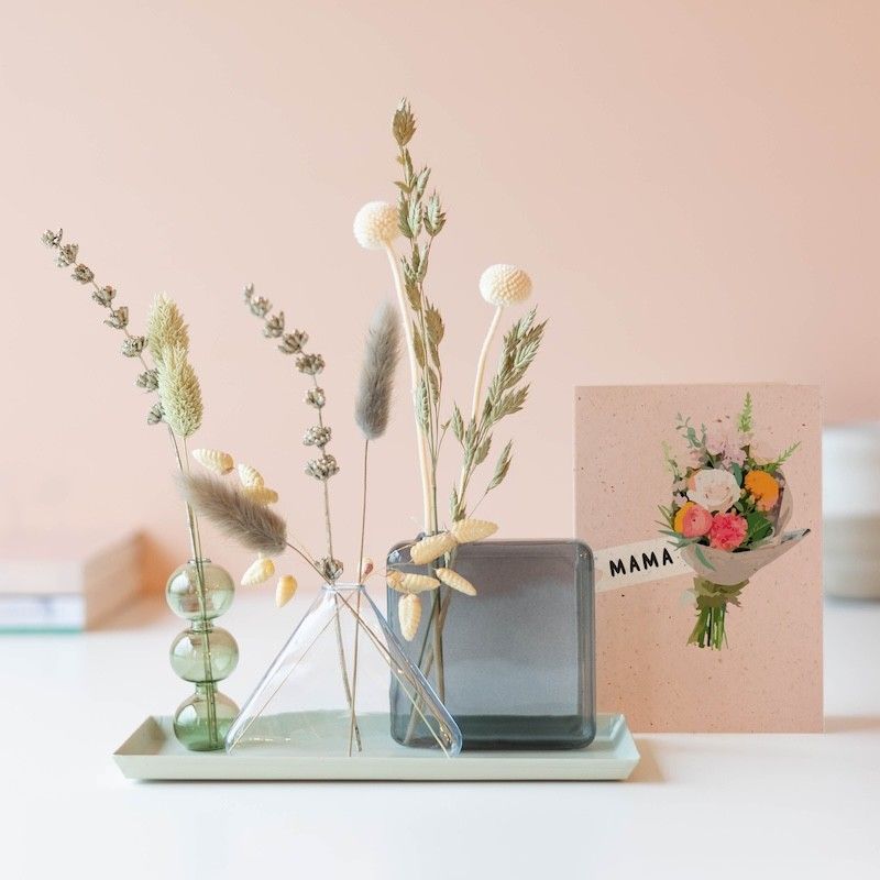 Verschillende vaasjes met naturel droogbloemen op een groen plateau met een wenskaart ernaast waar een boeket op staat met mam erbij geschreven
