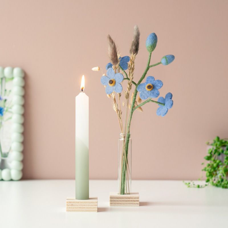 Een groen witte kaars met daarnaast een vaasje met blauwe vilten bloemetjes