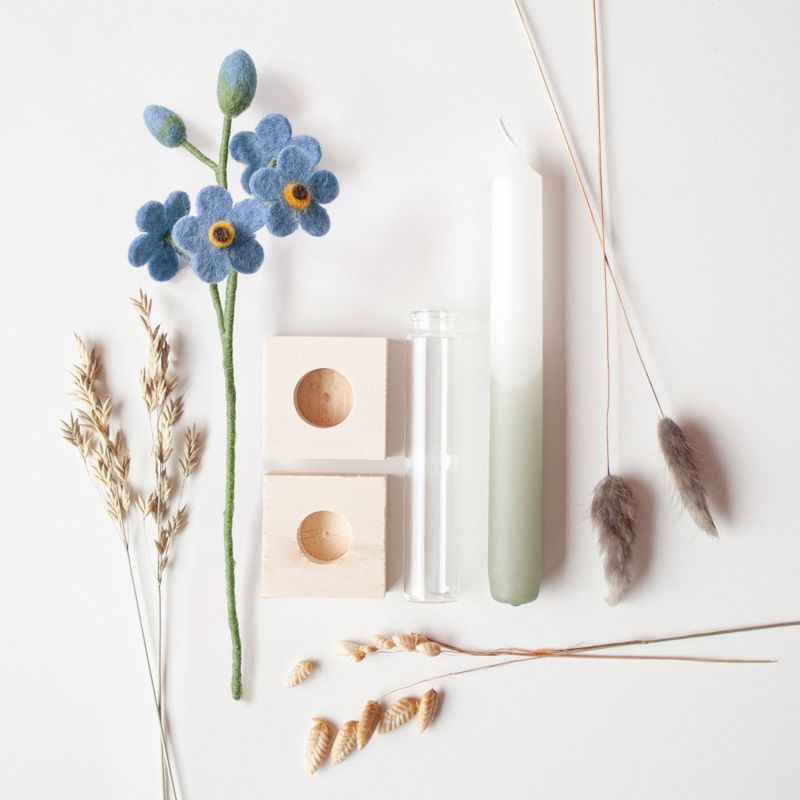 Een groen witte kaars met daarnaast een vaasje met blauwe vilten bloemetjes