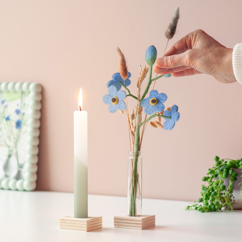 Een groen witte kaars met daarnaast een vaasje met blauwe vilten bloemetjes