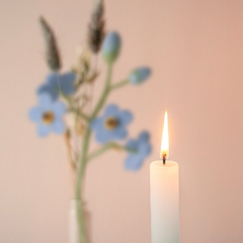 Een groen witte kaars met daarnaast een vaasje met blauwe vilten bloemetjes