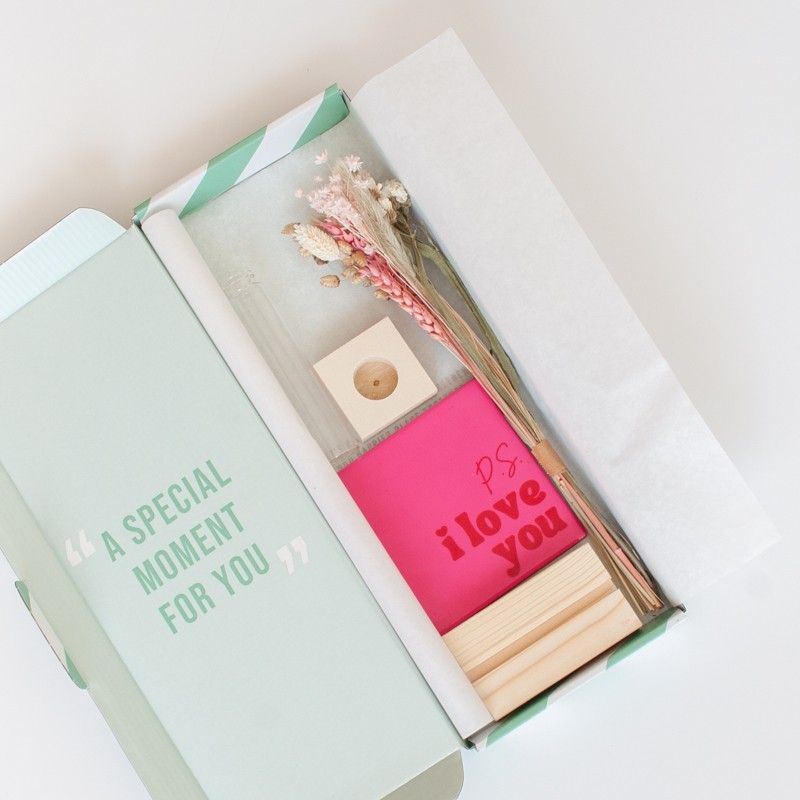 Roze tegeltje met tekst P.S. I love you met een houten standaard, een glazen vaasje, roze en naturel droogbloemen ernaast alles liggend in een brievenbusdoosje.