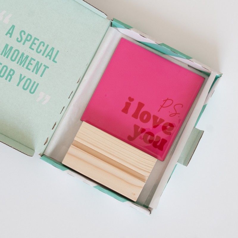 Roze tegeltje met P.S. I love you in rode letters met een houten standaard in een brievenbusdoosje