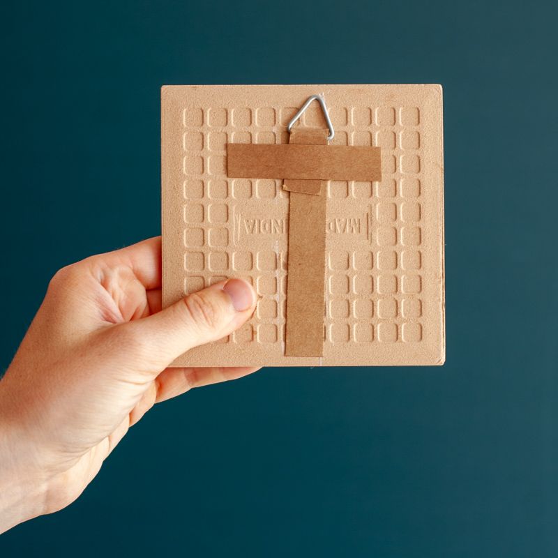 Cremekleurig tegeltje met in verschillende kleuren de tekst happy holidays. De tegel staat in een houten houdertje.