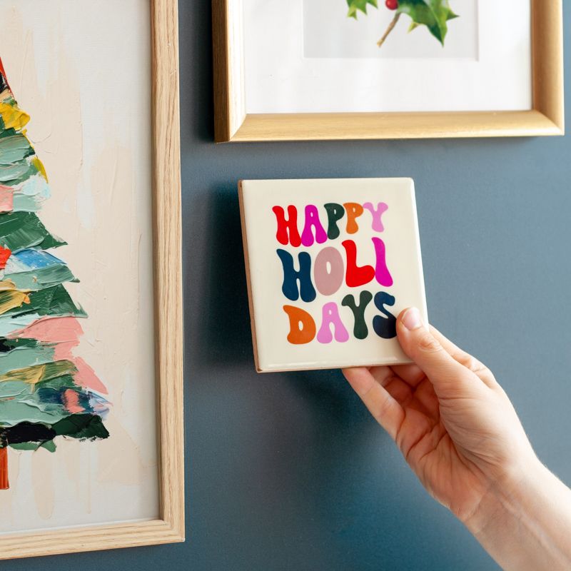 Cremekleurig tegeltje met in verschillende kleuren de tekst happy holidays. De tegel staat in een houten houdertje.