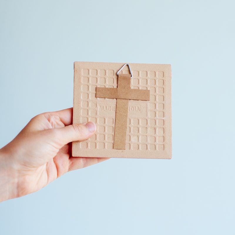 Kersttegel met de tekst "It's the most wonderful time of the year" in witte letters op een roze met rode achtergrond met golvend patroon. De tegel staat op een houten standaard.