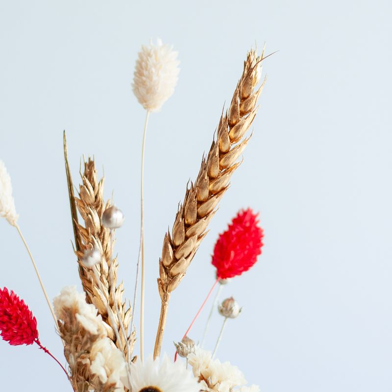 Kersttegel met de tekst "It's the most wonderful time of the year" in witte letters op een roze-rode golvende achtergrond. De tegel staat op een houten standaard naast een vaasje met droogbloemen in rood en wit kleuren.