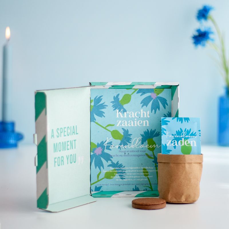 Blauw doosje met zaden van korenbloemen met de tekst kracht zaaien erop