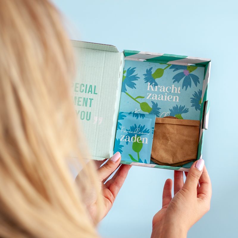 Blauw doosje met zaden van korenbloemen met de tekst kracht zaaien erop