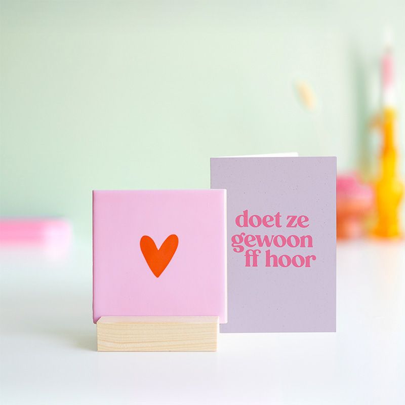 Roze tegeltje met in het midden een klein oranje hartje en het tegeltje staat op een houten houdertje