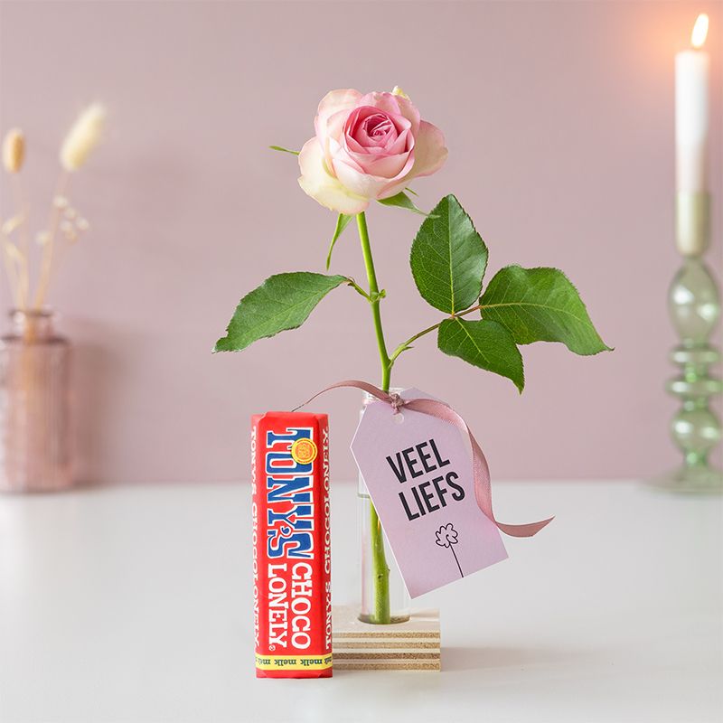Roze roos in vaasje met label veel liefs en een melk chocoladereep van Tony Chocolonely ernaast