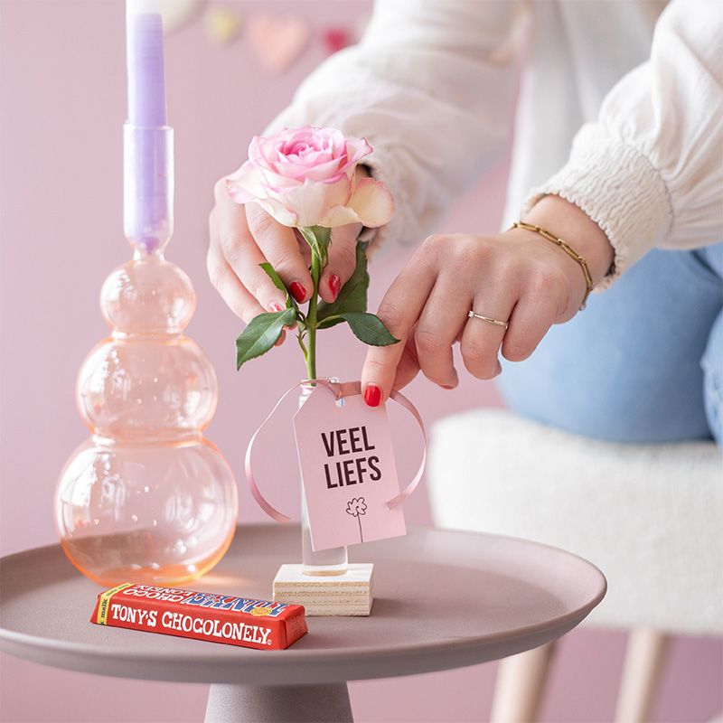 Roze roos in vaasje met label veel liefs en een melk chocoladereep van Tony Chocolonely ernaast