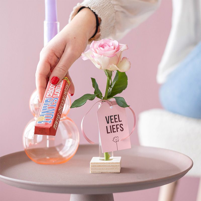 Roze roos in vaasje met label veel liefs en een melk chocoladereep van Tony Chocolonely ernaast