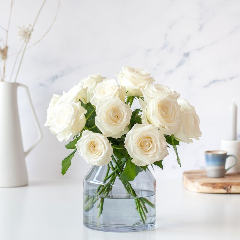 Vaas met witte rozen op een tafel.