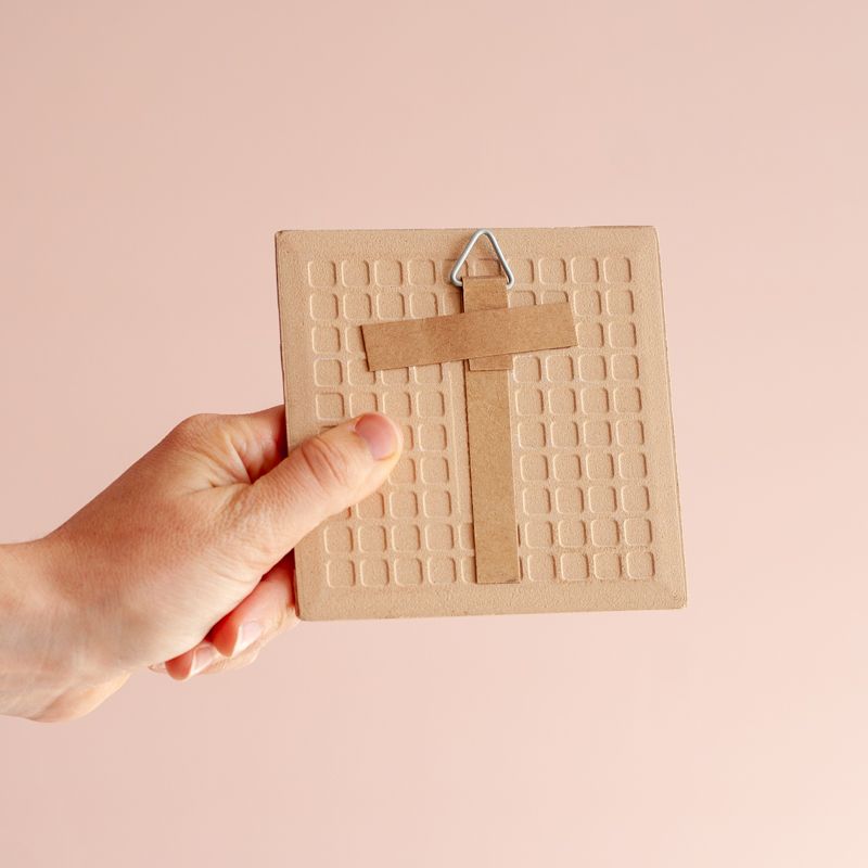 Licht roze tegeltje met in het rood de tekst love merry joyful bright peacefull cheerfull christmas holiday. De woorden staan onder elkaar en vormen een kerstboom. Boven het eerste woord staat een ster. Het tegeltje staat in een houten houder. 