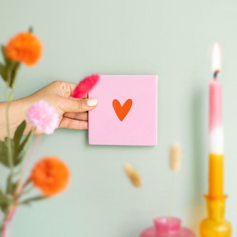 Roze tegeltje met in het midden een klein oranje hartje en het tegeltje staat op een houten houdertje