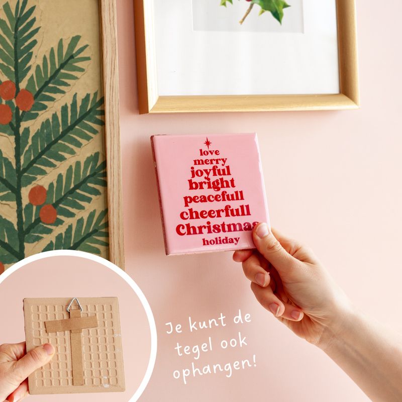 Roze kersttegel met in het rood gelukswensen in kerstboomvorm geschreven met een vaasje droogbloemen ernaast. Beiden staan in een houten blokje